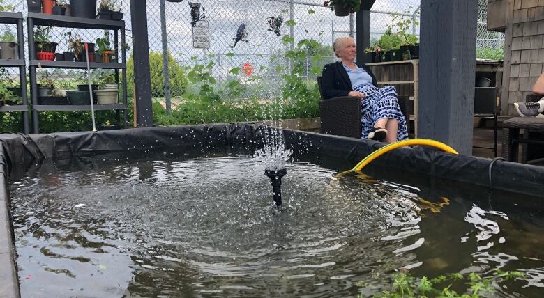 Woman sits in a chair alongside a water fountain. 