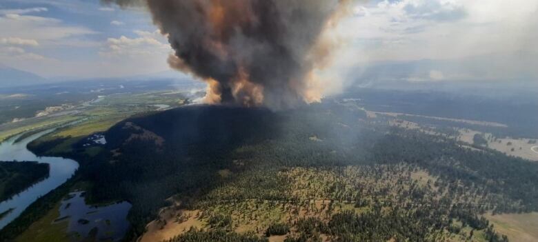 Thick brownish grey smoke rises into the air above a green and yellow landscape.