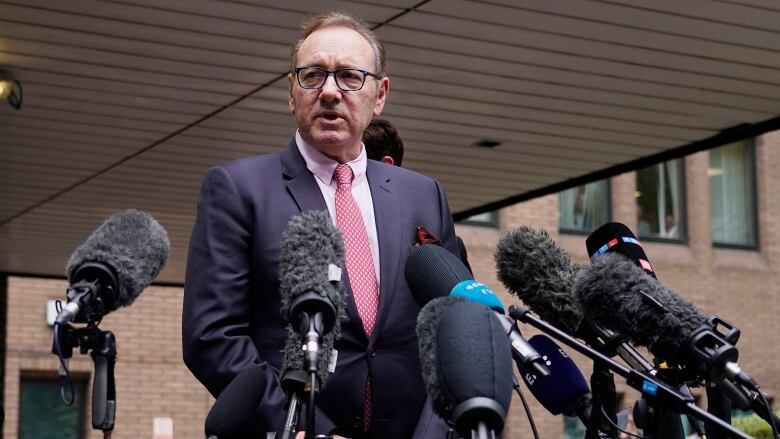 A man speaks into several microphones during a media scrum.