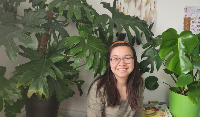 A woman grins at the camera, framed by two large tropical plants. 