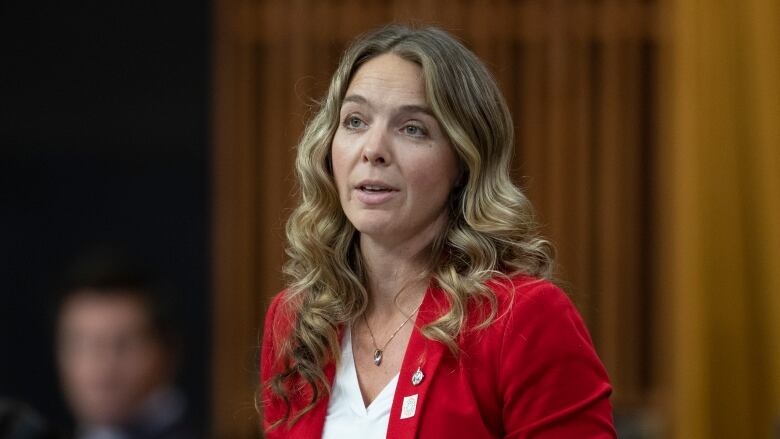 MP Jenna Sudds rises in the House of Commons. She's wearing a red blazer and white blouse.