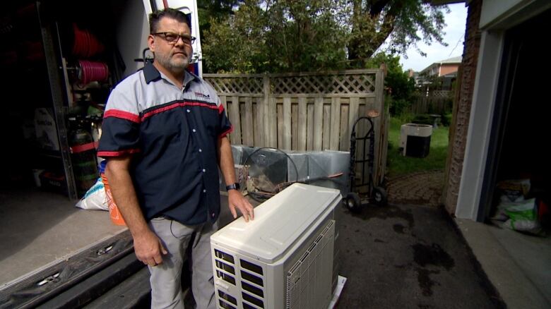 The owner of a heating and cooling company stands in front of a service van and beside a new heat pump unit.