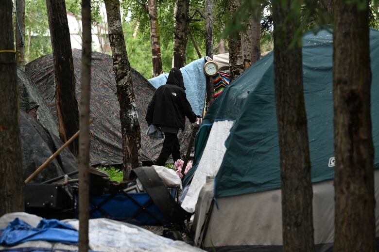 A person is seen walking through a group of tents in the trees.