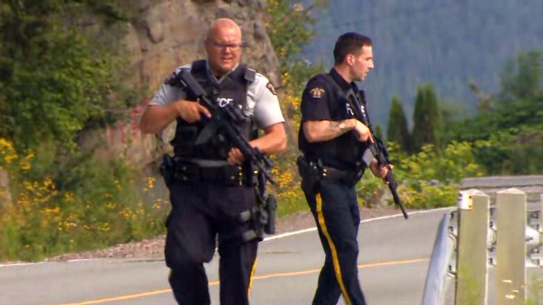 Two police officers with assault weapons walk toward a bridge.