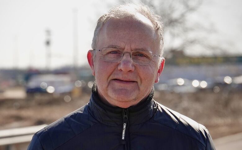 An older man standing outside wearing a black zip-up jacket