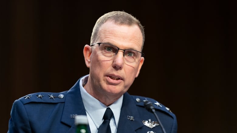 Man in blue military uniform with lots of medals, in front of dark background