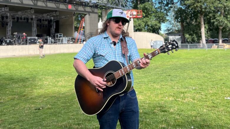 A man in a light-blue shirt and dark blue jeans is pictured playing the guitar.