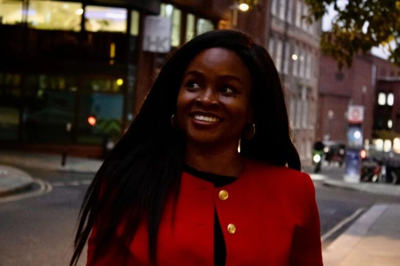 A woman smiles outside at an urban street intersection. 