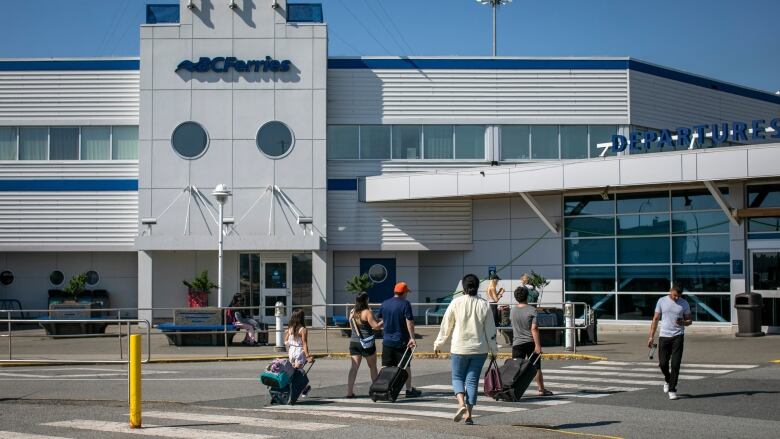 People are pictured wheeling suitcases on their way to a B.C. Ferries terminal.