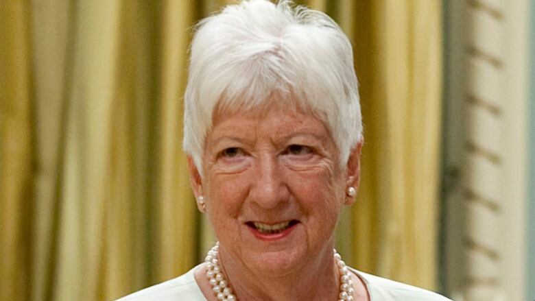 A smiling woman with short white hair, wearing pearl earrings and matching pearl necklace