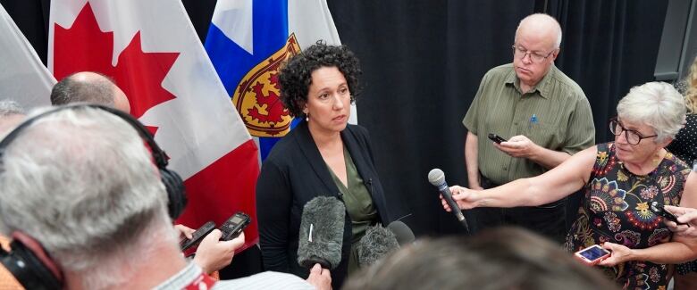 A woman is ringed by reporters holding microphones.