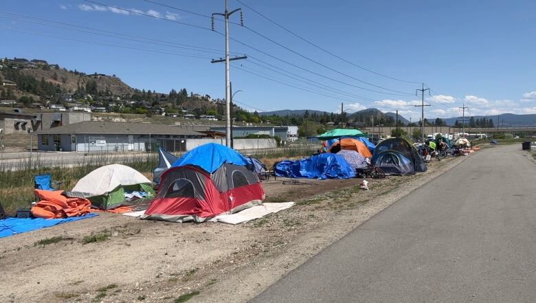 A line of tents situated along a road with utility poles and a hill in the background.