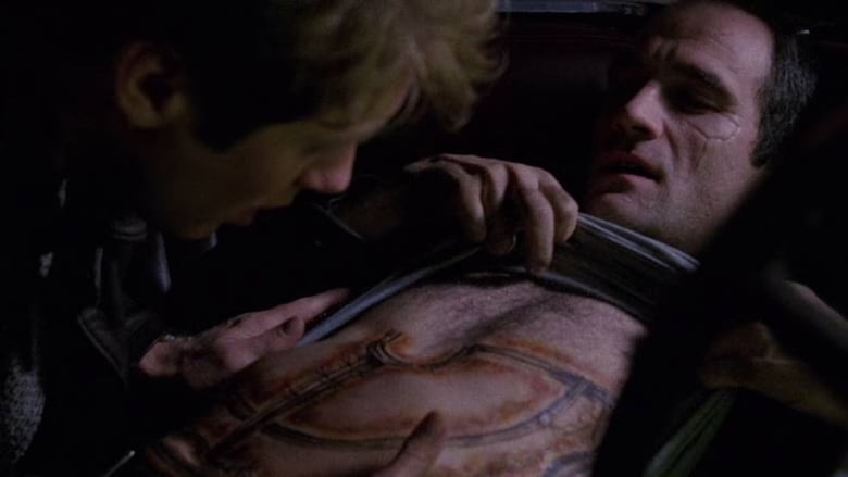 A still frame from the film Crash. Elias Koteas pulls his shirt up to reveal a medical tattoo as James Spader touches his chest.