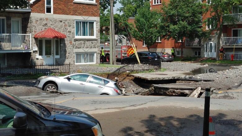 A car partially sunk into a large crater in the pavement. 