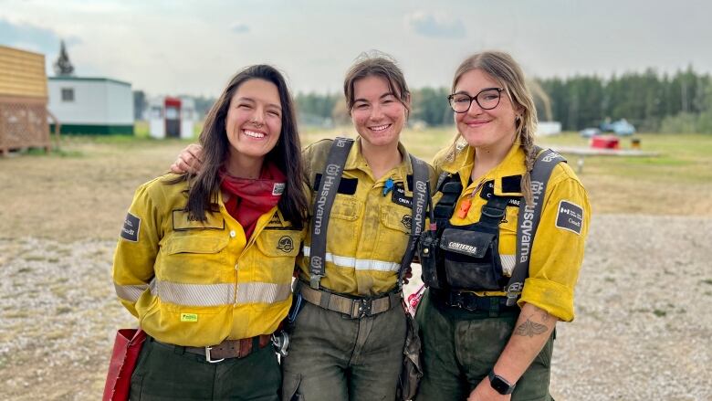 Three women in firefighting gear pose for a photo.