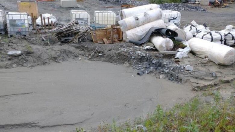 Piles of containers and scrap material are piled beside a muddy drainage sump.