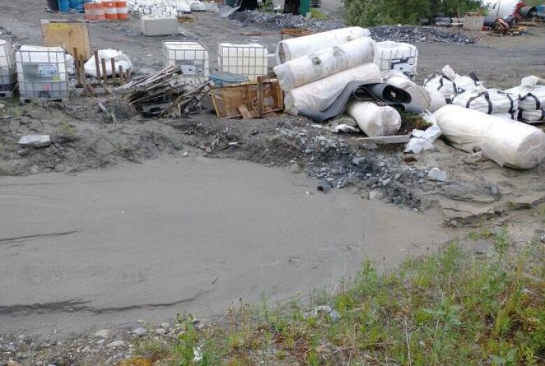 Piles of containers and scrap material are piled beside a muddy drainage sump.