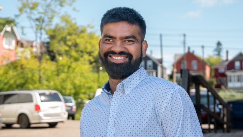 A man wearing a dress shirt stands outside and smiles.