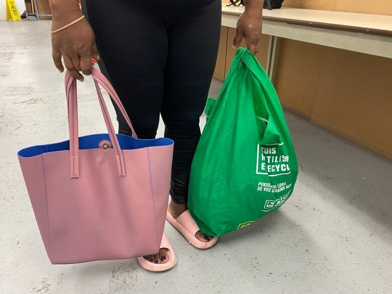 A woman in pink slides holds a pink bag and a dollarama reusable bag filled with groceries. The picture is taken from the waist down. 