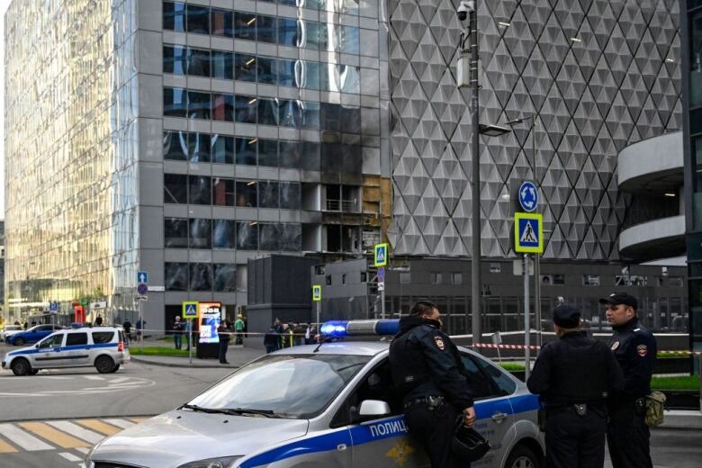 Police in the forefront stand near an office building with burnt-out windows.