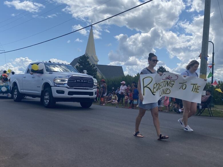 Parade participants carry a sign that says Reconnecting With The Land,