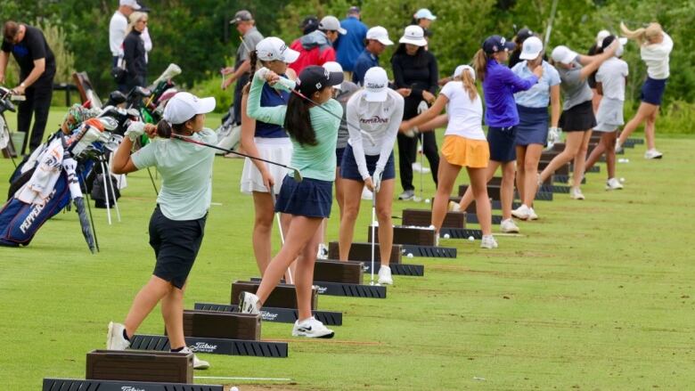 A line of golfers practice their swing on the driving range at Ashburn Golf Club. 