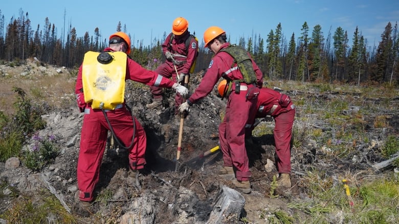 People dig in smoking soil, wearing red coveralls. 