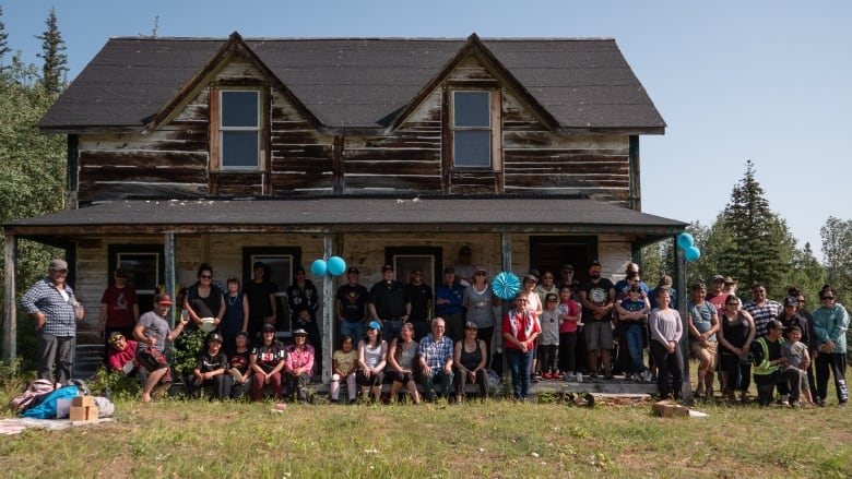 A large group of people poses in front of a two-storey log building.