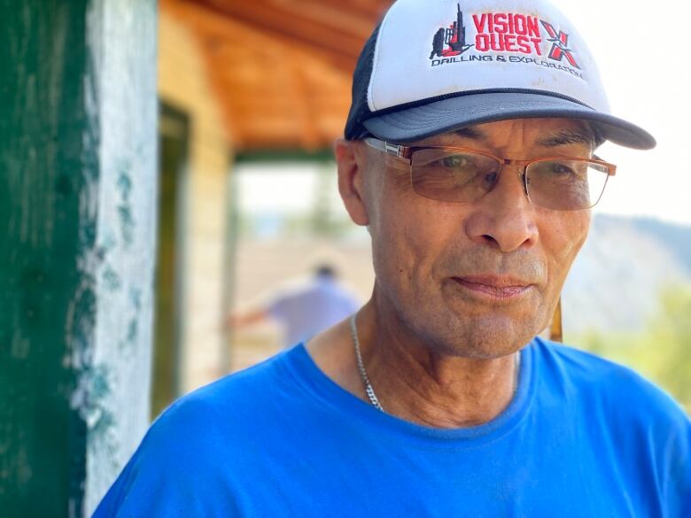 Portrait of an older man in a hat, glasses and blue shirt.