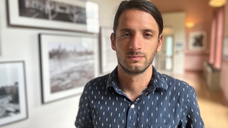 A man in a blue shirt stands in front of a wall of black and white photos. 