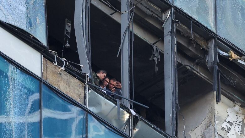 Three men are seen in a window of a large building, where the glass has been blown out.