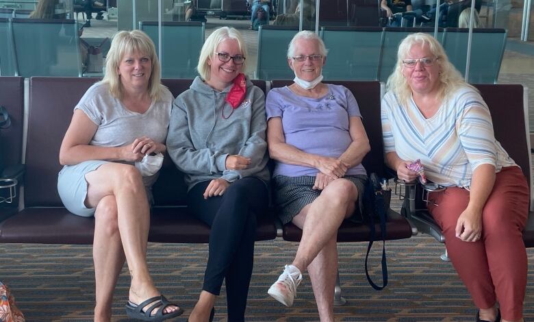 Four women with blond hair sit side by side on a purple bench, looking into the camera.