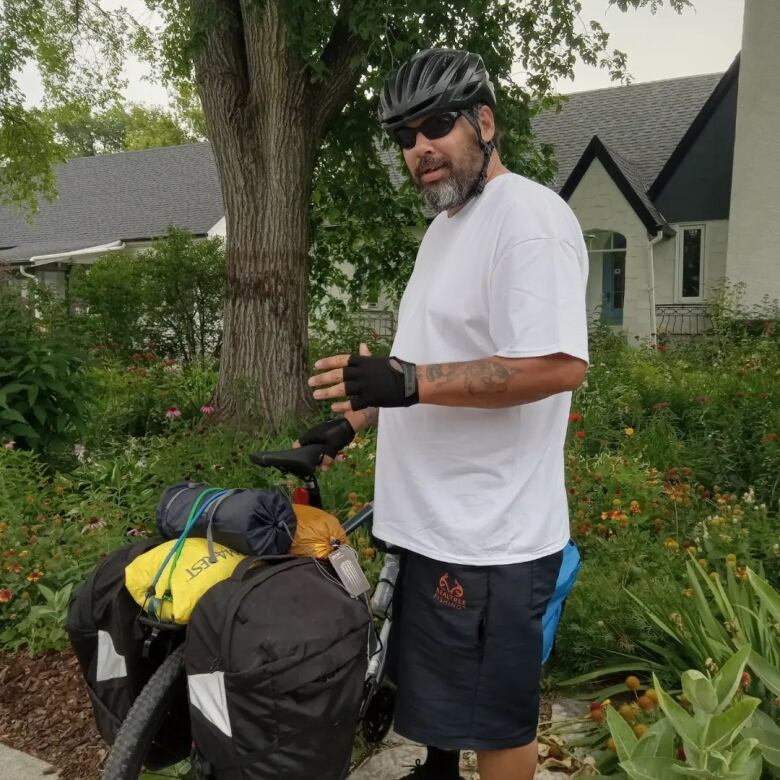 A man in a white T-Shirt and shorts, standing next to a bike.