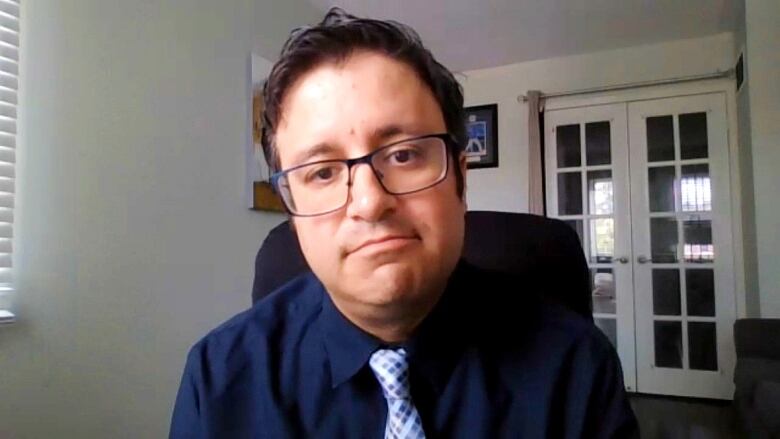 A man in a navy shirt and tie looks into a webcam.