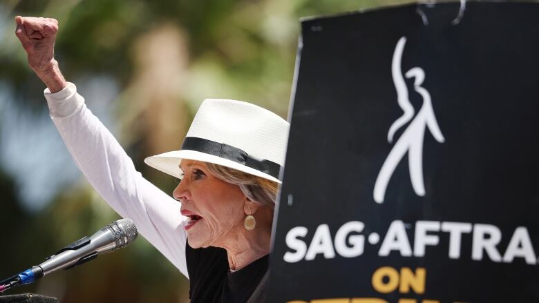 Jane Fonda holding a fist in the air and speaking to a crowd outside a Netflix studio in Los Angeles.