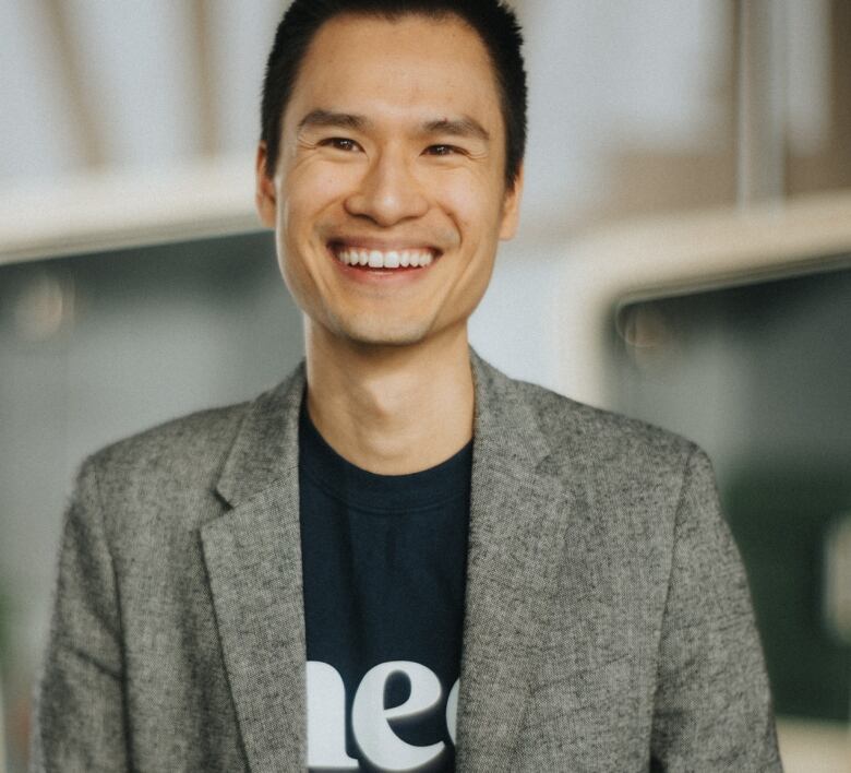 a man wearing a black t shirt and grey sport coat sits on a chair and smiles