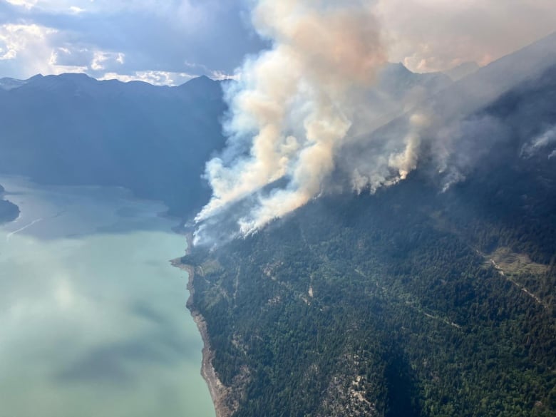 Smoke rise from a hilltop next to a lake.