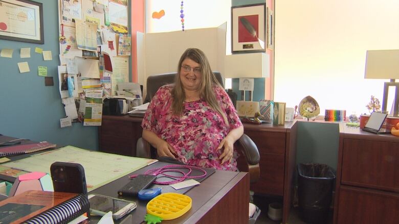 A woman in pink floral dress sits at a table in an office.