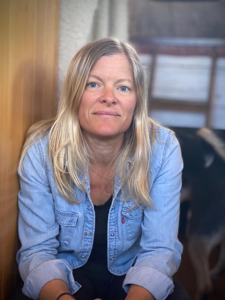 A woman with long blond hair wearing a blue shirt sits facing the camera.