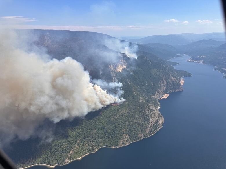 Plumes of smoke rise from a lakeside hilltop.