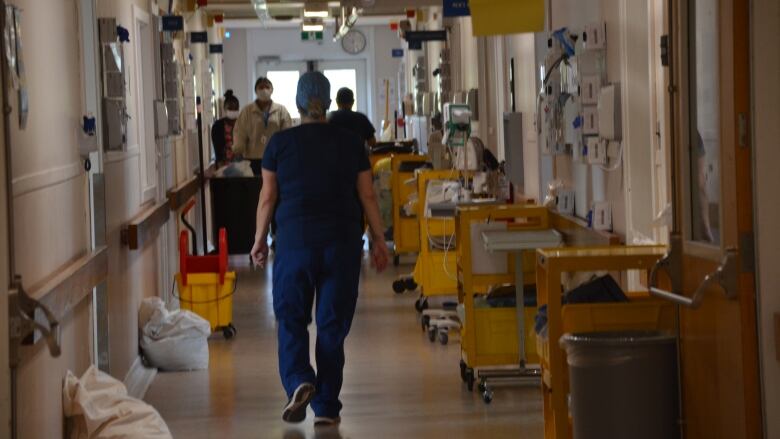 a doctor walks down a crowded and dimly lit hospital hallway 