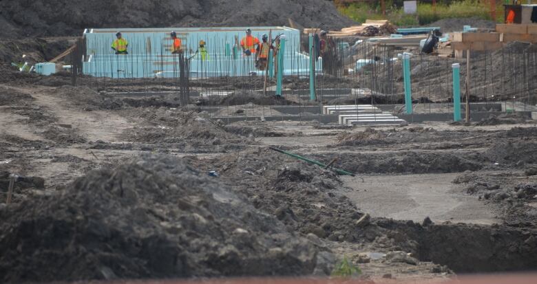 pipes and rebar poke out of piles of dirt, with construction workers in the background 