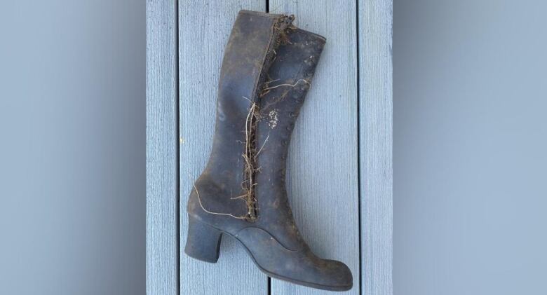 A black, rubber high-heeled boot lays on its side. The zipper is open and twigs are protruding.