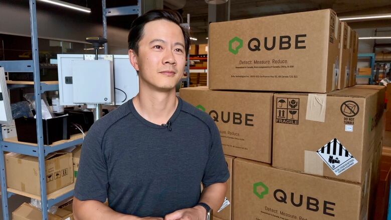 A company executive stands in front of a pile of boxes packaged up with new equipment to be shipped to customers.