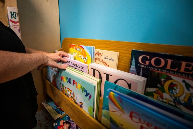 Children's books are shown on a shelf with the titles 'I Am A Rainbow' and 'Pride Puppy'.