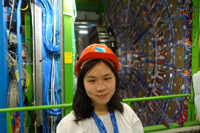 A woman wearing a helmet in an underground tunnel filled with blue and red electrical cable