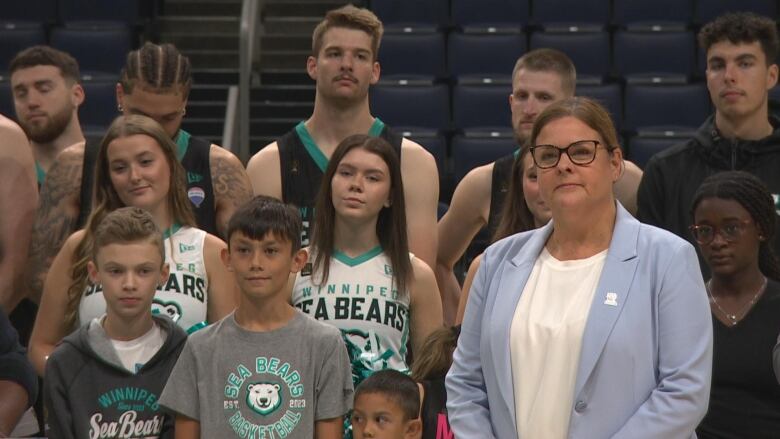 A woman stands with children and basketball players.