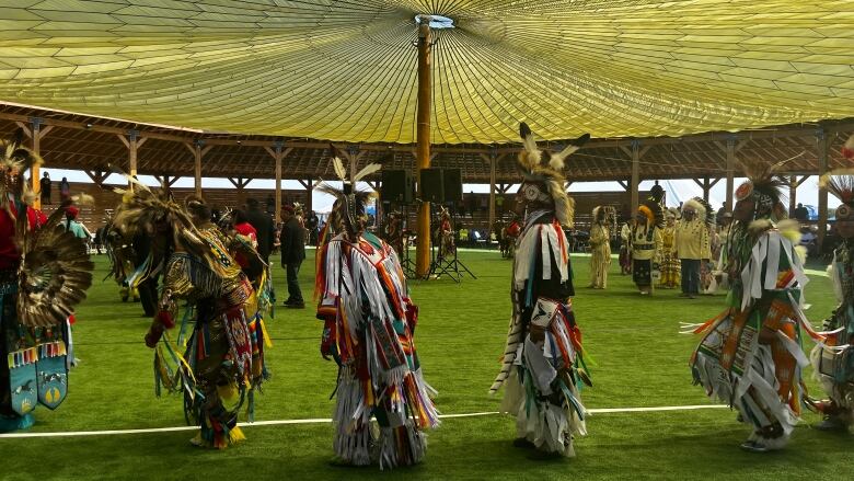 Powwow dancers can be seen wearing regalia and dancing under an arbour. 