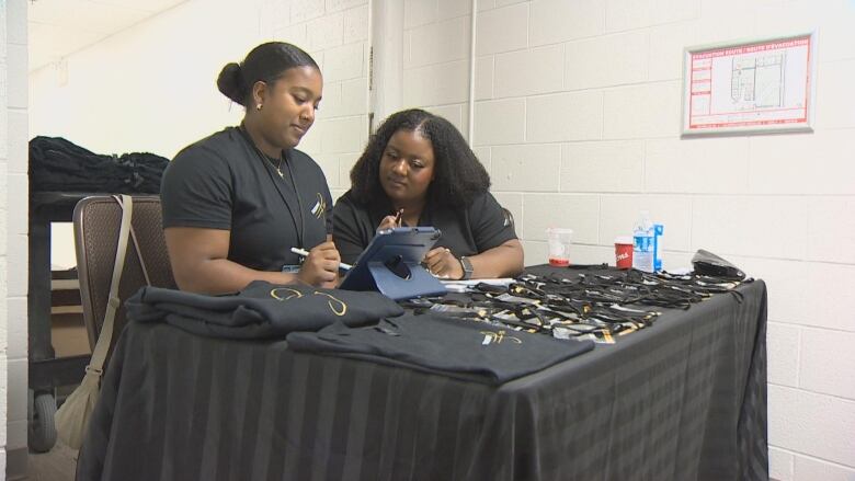 Two Black women sit at a table in front of an iPad.