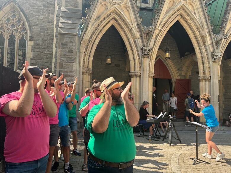 A choir wearing colourful shirts sing outside of a cathedral.